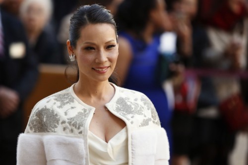  Lucy Liu smiles warmly while wearing an elegant, detailed white outfit with a stylish coat at a public event.