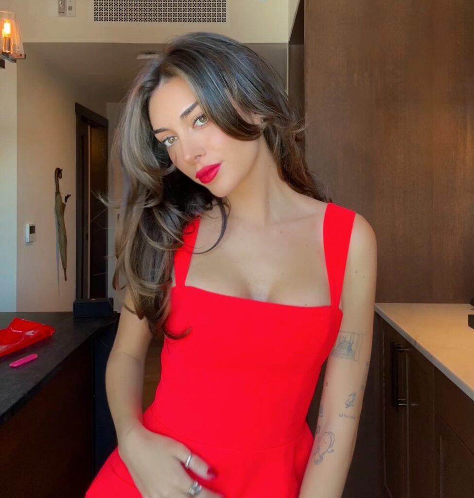 A young woman with long, flowing hair poses in a bright red dress, showcasing her confident smile and bold red lipstick.