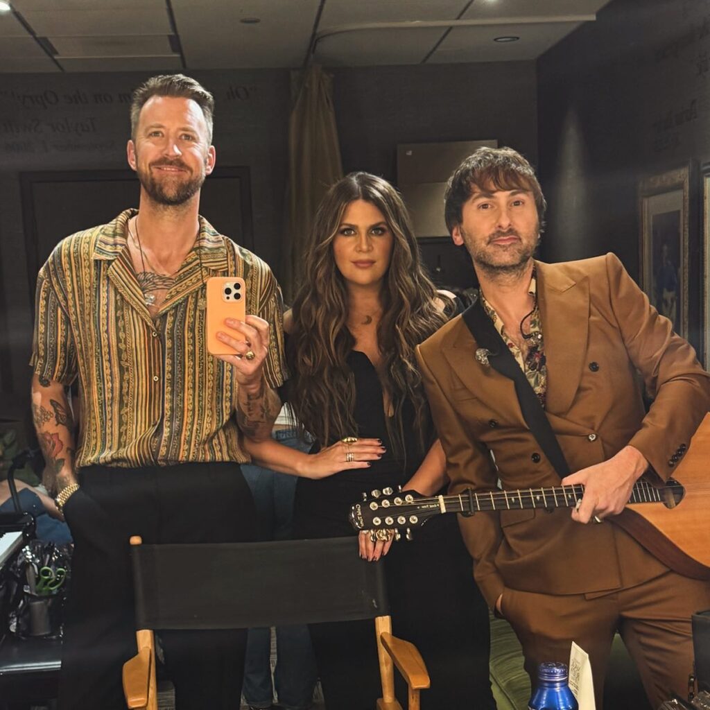 Charles Kelley and Lady A members posing together backstage, smiling and embracing their musical bond.