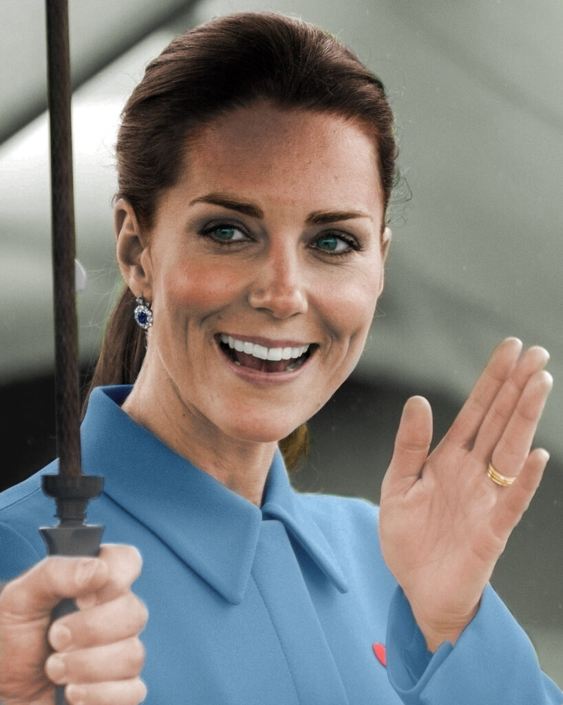 A smiling woman with long brown hair wearing a blue coat waves while holding an umbrella. She has blue earrings and appears to be in a cheerful mood.