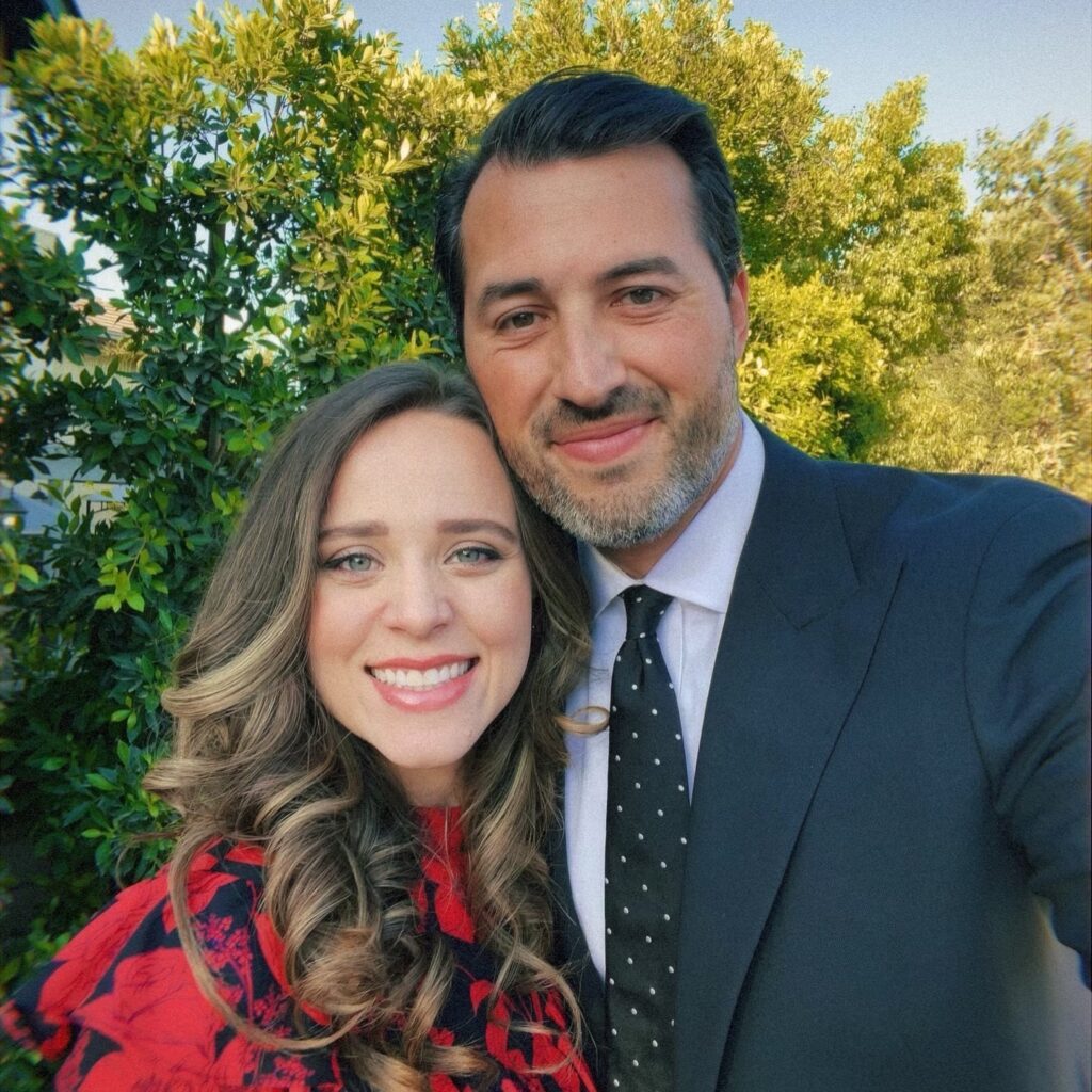 Jinger Duggar and Jeremy Vuolo smiling together in a close-up selfie, surrounded by lush greenery.