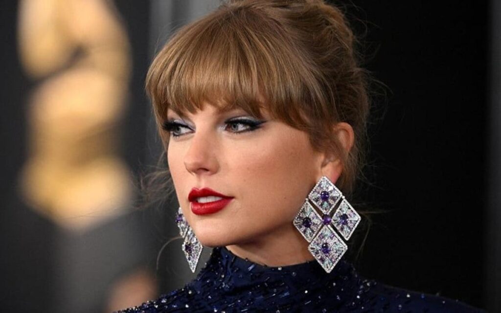 Taylor Swift poses elegantly with glamorous makeup and large diamond earrings at a red carpet event.