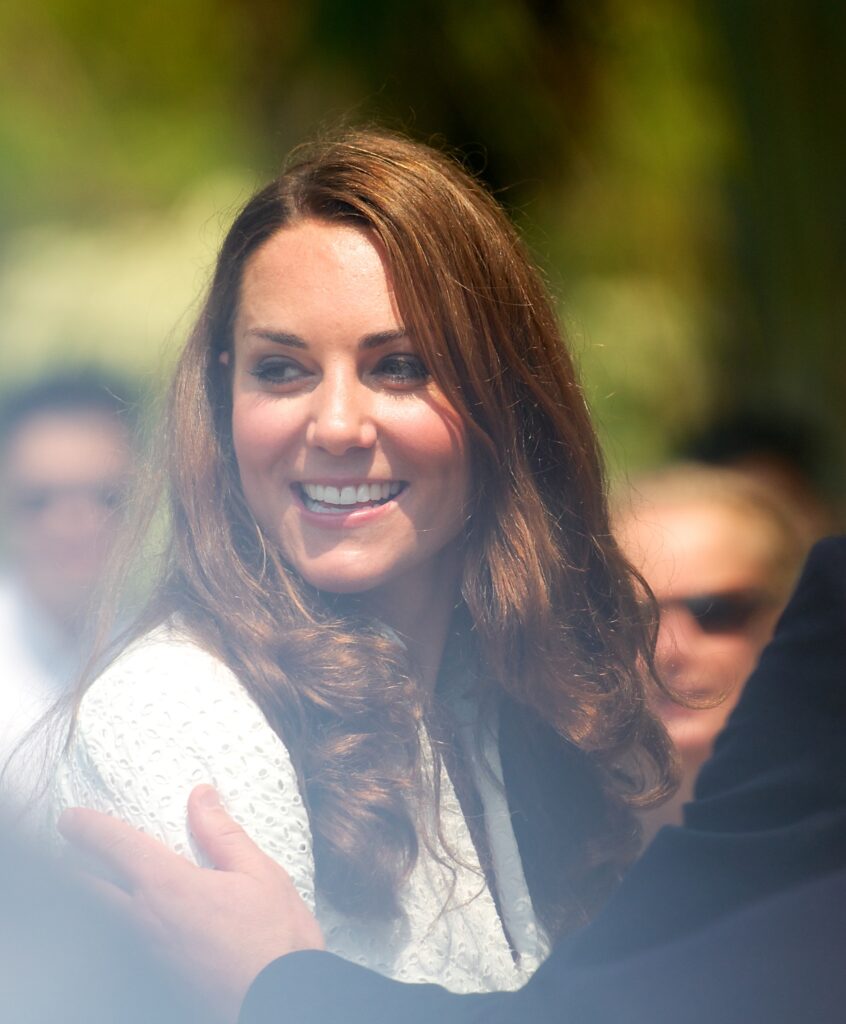 Kate Middleton smiling warmly during a public appearance, wearing a white outfit with long, wavy hair and a cheerful expression.