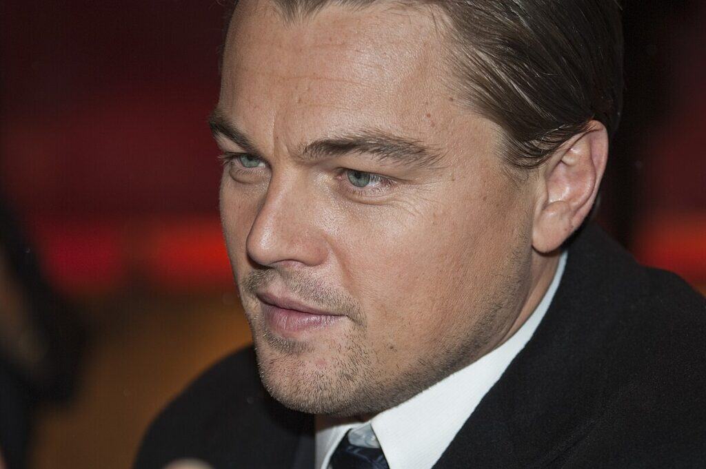  Leonardo DiCaprio Close-up of a man in formal attire at an indoor event, warm red-orange blurred background.