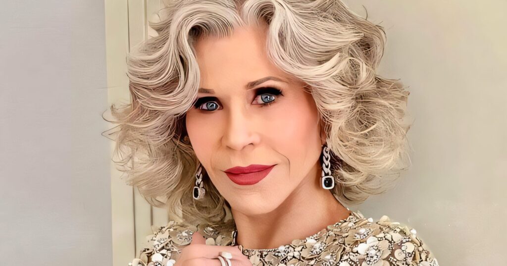 Elegant older adult with silver curls wearing a beaded floral top, posing indoors with jewelry and soft makeup.