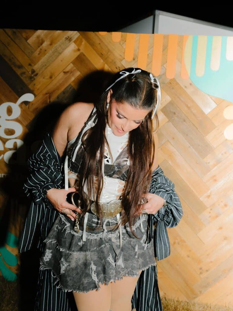 Nelly Furtado looks down adjusting her outfit featuring a pinstripe jacket and distressed skirt.