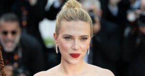 Scarlett Johansson at a formal event wearing elegant jewelry and bright lipstick, posing for cameras.