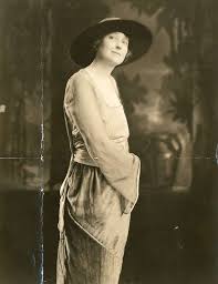 An oil portrait of an Edwardian-era woman, Mrs. Charles S. Carstairs, by John Singer Sargent. She wears an elegant white satin gown and a large feather boa, holding a fan while standing next to a classical pillar and looking directly at the viewer.