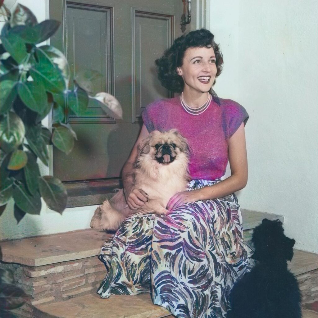Close-up of an older, smiling Betty White holding two small dogs: a tan Pomeranian mix and a light-colored Chihuahua mix.