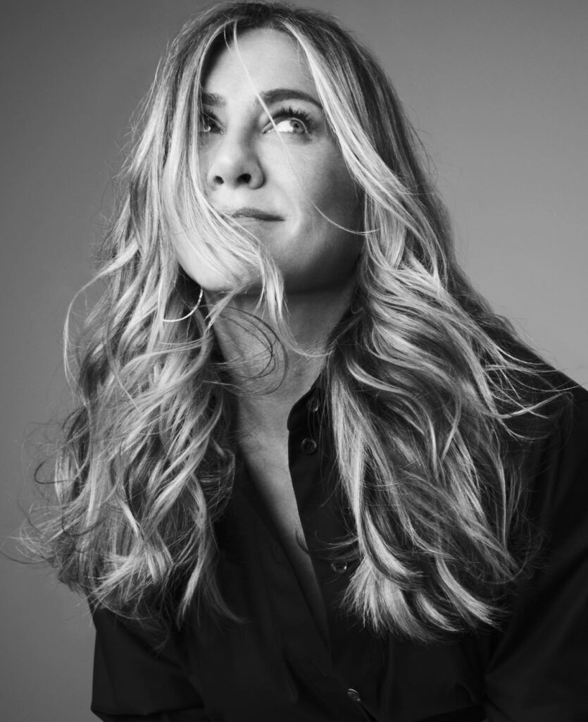 Black and white close-up portrait of a blonde woman with wavy hair blowing across her face, looking up and to the side.