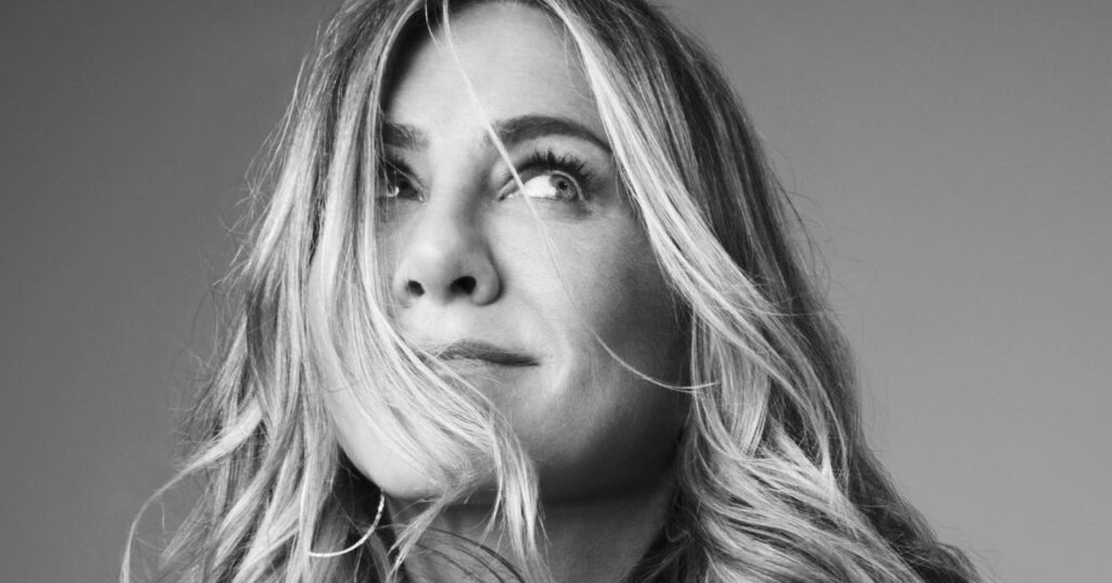 Black and white close-up portrait of a blonde woman with wavy hair blowing across her face, looking up and to the side.