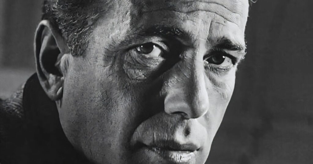 A high-contrast, black and white close-up portrait of Humphrey Bogart, showing detailed facial textures and a thoughtful, intense expression.