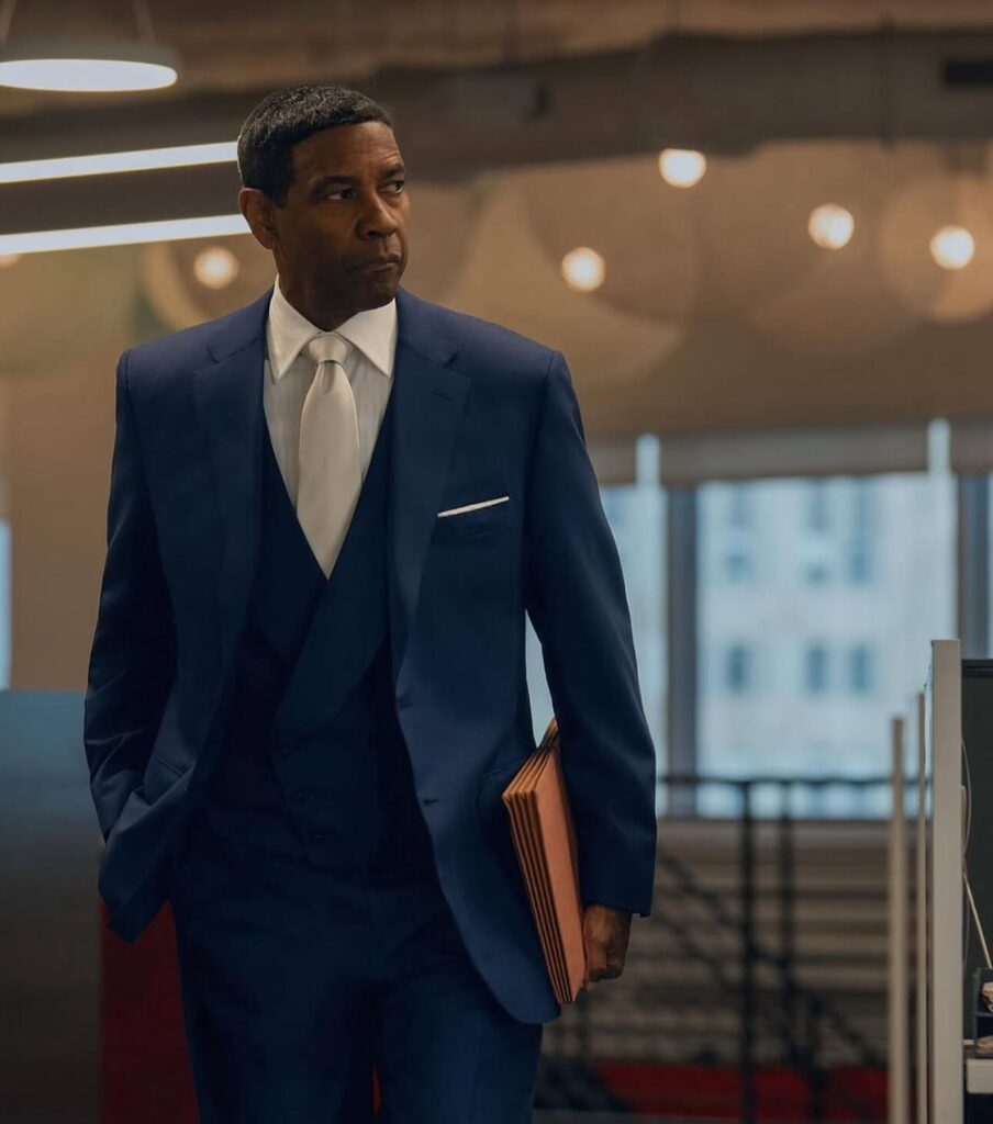  A male singer in a long dark coat performs onstage under dramatic blue lighting and fog, holding a microphone with one hand while gesturing with the other.