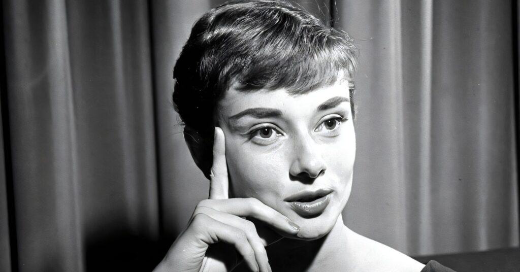 A black and white candid photo of Audrey Hepburn looking down while reading a magazine titled "Eau de Lanvin for Men."