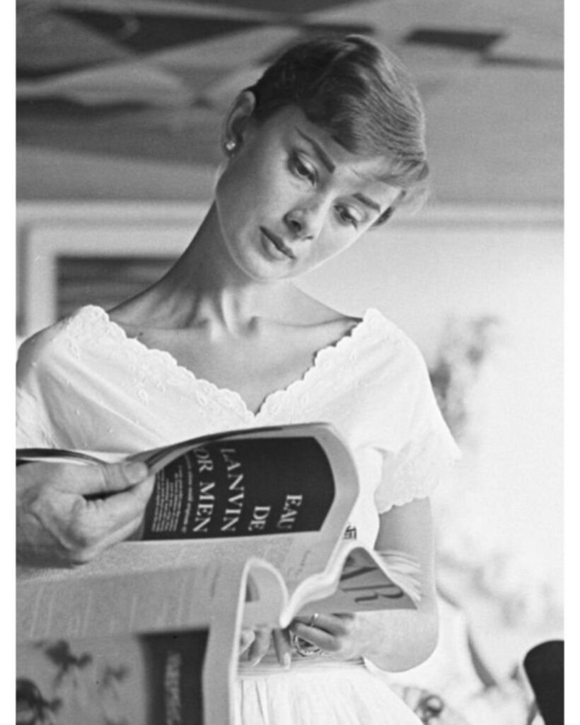 A black and white studio portrait of Audrey Hepburn resting her chin on her hand, looking thoughtfully off-camera.