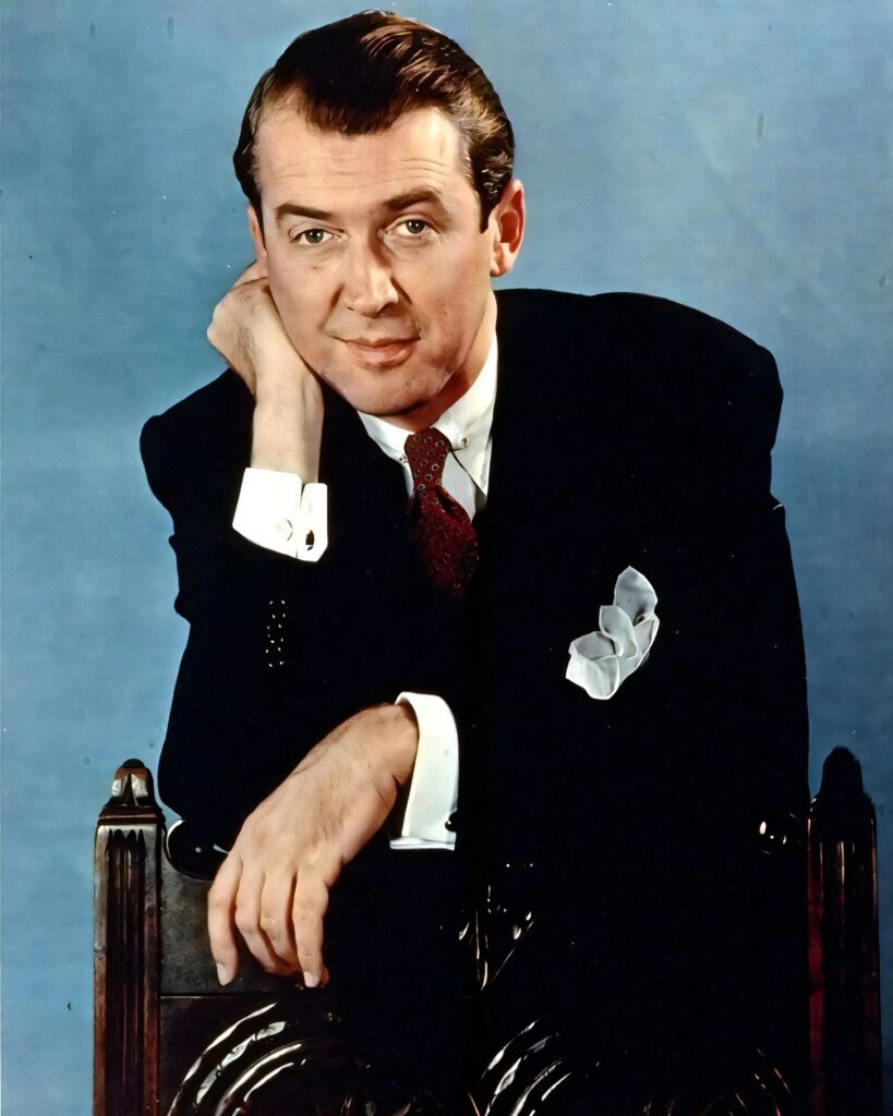 A colorized vintage portrait of a man in a dark suit and red tie, resting his head on his hand.