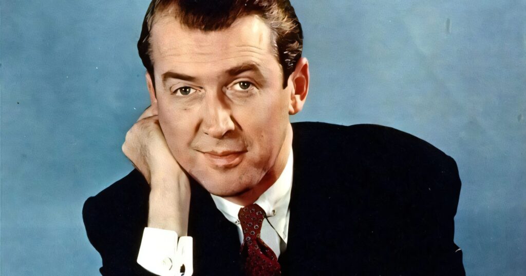 A colorized vintage portrait of James Stewart in a dark suit and red tie, resting his head on his hand.