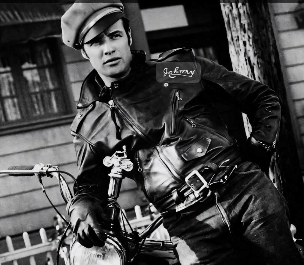 A black and white photo of Marlon Brando as Johnny Strabler, leaning on a motorcycle in a leather jacket.