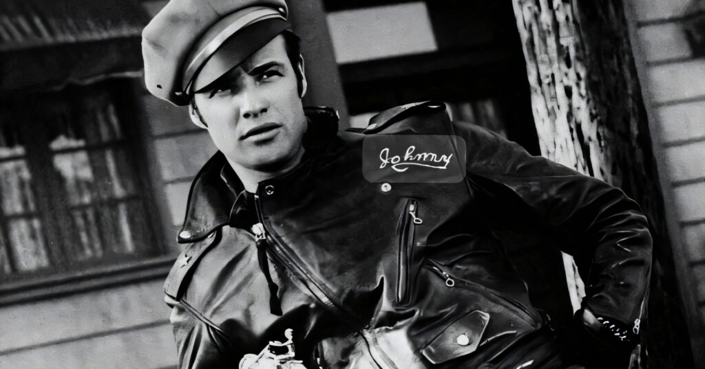 A black and white photo of Marlon Brando as Johnny Strabler, leaning on a motorcycle in a leather jacket.