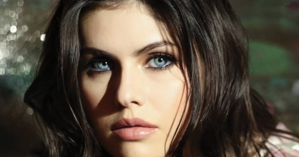 A dramatic close-up headshot of Alexandra Daddario with her signature blue eyes and wavy dark hair.