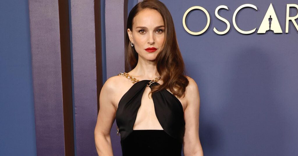 Natalie Portman wearing a sleek black halter-style gown with gold chain detailing at a Governors Awards red carpet event.