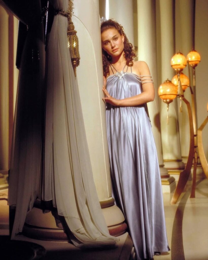 Natalie Portman as Padmé Amidala in a lilac satin gown, leaning against a white pillar in a Naboo palace setting.