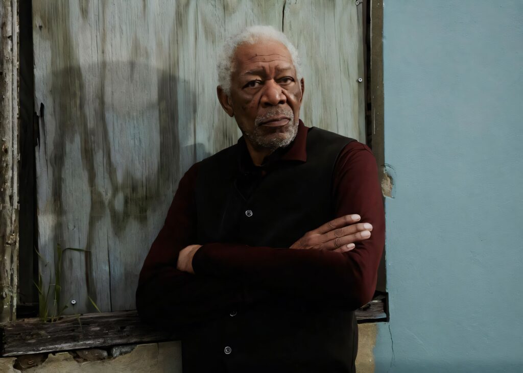 A somber, high-contrast photograph of actor Morgan Freeman standing with his arms crossed against a weathered wooden background.